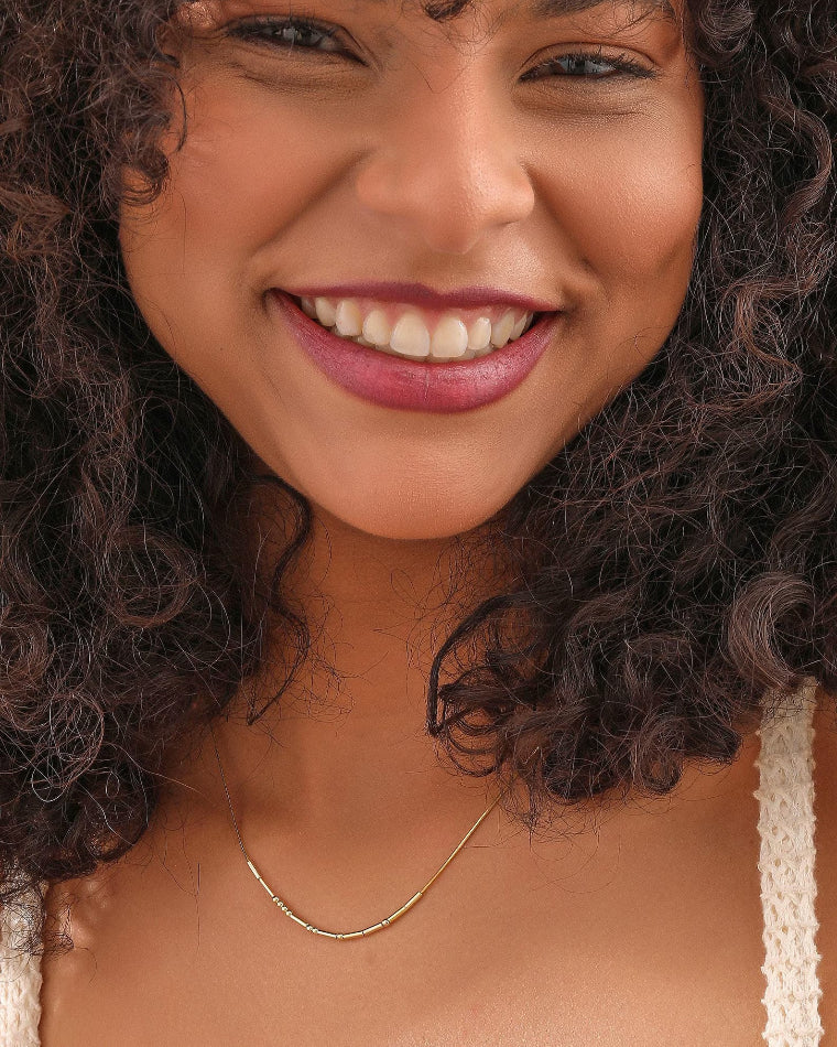 Blancora morse code gold chain necklace and a cream lace-trim top.